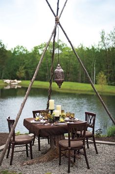 an outdoor dining table set up with candles, plates and utensils under a teepee