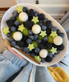 a white bowl filled with blackberries, grapes and kiwis next to a pair of blue gloves