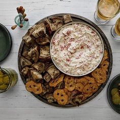 a platter filled with crackers and dip surrounded by other snacks on the table