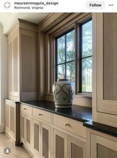 a vase sitting on top of a counter in front of a window next to wooden cabinets