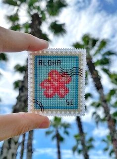 someone is holding up a small cross stitched stamp with the word aloha on it