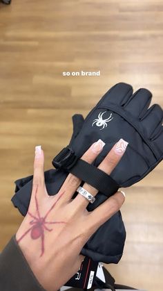 a woman's hand with a spider tattoo on it holding up her black gloves