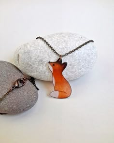 a necklace with an orange fox on it sitting next to two rocks and a chain