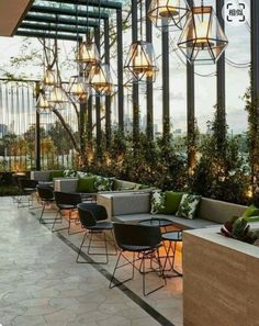 an outdoor seating area with lots of plants and lights hanging from the ceiling above it