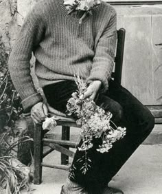 black and white photograph of a man sitting on a bench with flowers in his hand