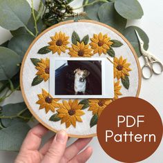 a hand holding up a embroidery hoop with sunflowers and a dog on it