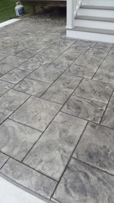 an outdoor patio with grey tiles and steps leading up to the front door, grass in the background