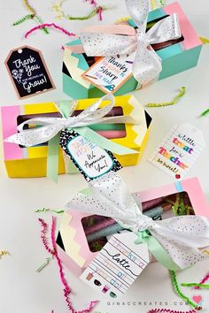 three colorful boxes with ribbons tied around them on a white surface and some confetti sprinkles in the background