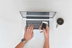 a person typing on a laptop with their cell phone