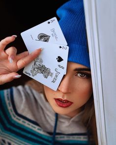 a woman wearing a blue hat and holding playing cards up to her face with both hands