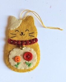 a cat ornament hanging from a string on a white surface with red and orange buttons