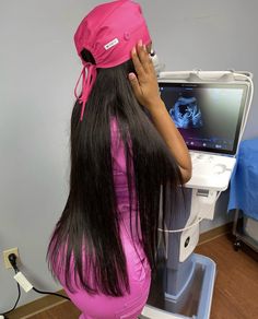 a woman with long black hair sitting in front of a computer monitor wearing a pink hat