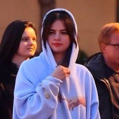 a woman wearing a white hoodie is walking down the street with other people behind her