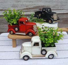 three toy trucks with plants in them sitting on a table next to a wooden bench