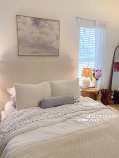 a bed with white sheets and pillows in a bedroom next to a dresser, mirror and lamp