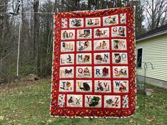 a red and white quilt hanging from the side of a house in front of trees