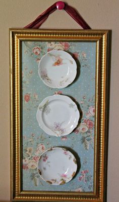 two plates are hanging on a wall in front of a framed picture with floral designs