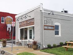 the outside of a coffee shop with a painted mural on the wall and picnic tables in front