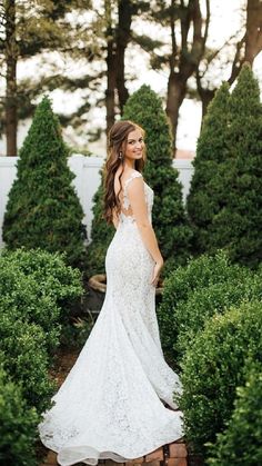 a woman in a white wedding dress is posing for the camera while surrounded by bushes