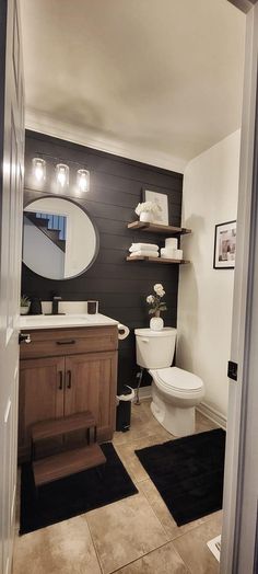 a bathroom with black and white tile flooring and wooden cabinetry, along with a round mirror on the wall