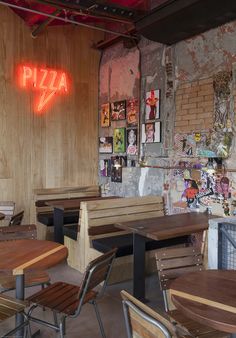 a restaurant with wooden tables and chairs in front of a neon sign that reads pizza