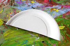 a white paper plate sitting on top of a colorful painting covered table with lots of paint