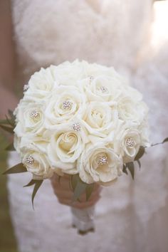 the bride's bouquet is made up of white roses and diamond brooches