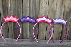 three purple, pink and white headbands with tiaras on them sitting next to a wooden fence