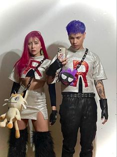 two people dressed in costumes standing next to each other holding cell phones and looking at them