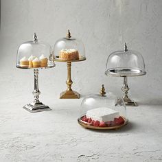 three desserts under glass dome covers on trays with plates and cake stands in the background