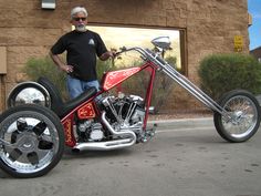 a man standing next to a red and black chopper bike