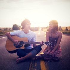 two young people sitting on the side of a road with an acoustic guitar in front of them