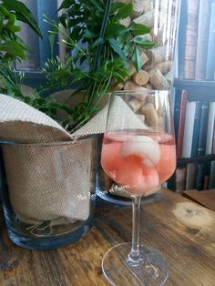 a glass filled with liquid sitting on top of a wooden table next to a potted plant