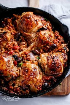 a skillet filled with chicken and rice on top of a wooden cutting board