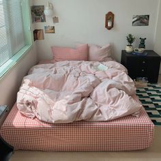 an unmade bed with pink sheets and pillows in a room next to a window