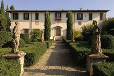 an old house with statues in front of it and bushes around the walkway leading up to the entrance