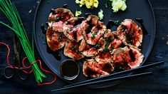 some meat and vegetables on a black plate with chopsticks next to the plate