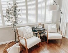 a living room with two white chairs and a coffee table in front of the window