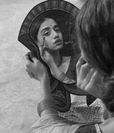 a woman is looking at herself in the mirror while she brushes her face with a brush