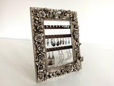 an ornate silver frame with earrings hanging from it's sides on a white table