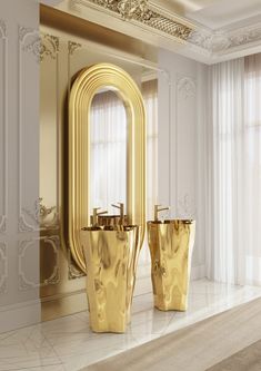 two gold vases sitting on top of a white counter next to a large mirror