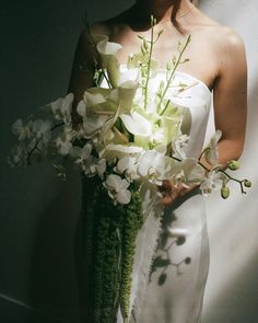 a woman in a white dress holding a bouquet of orchids and greenery on her wedding day