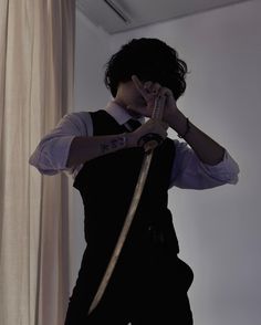 a man in black vest talking on cell phone next to window with curtain behind him