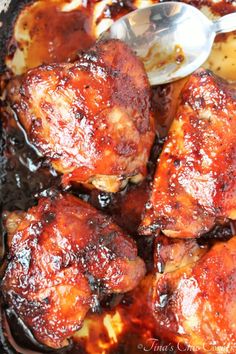 chicken thighs covered in bbq sauce with a spoon sitting on top of the skillet