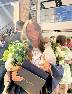 a woman in graduation gown holding flowers and a book