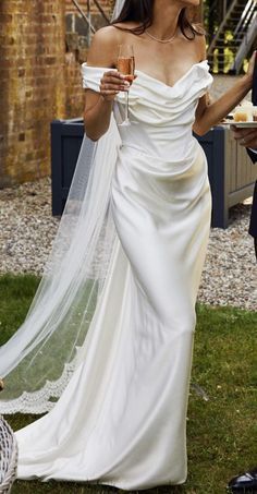 a woman in a white wedding dress holding a glass of wine while standing next to a man