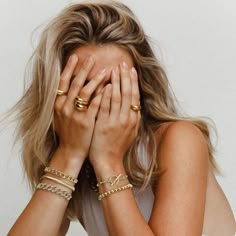 a woman covering her face with both hands while wearing gold rings and bracelets in front of her face