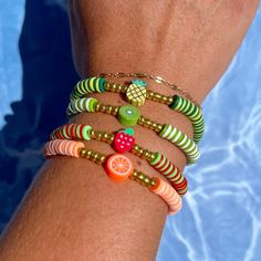 a woman's arm wearing bracelets with fruit and bead designs on them