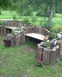 a wooden bench made out of logs in the middle of a grassy area with flowers and trees around it