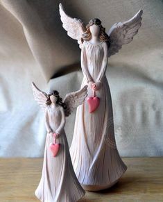 two ceramic angel figurines with hearts on their hands, one holding the other's hand